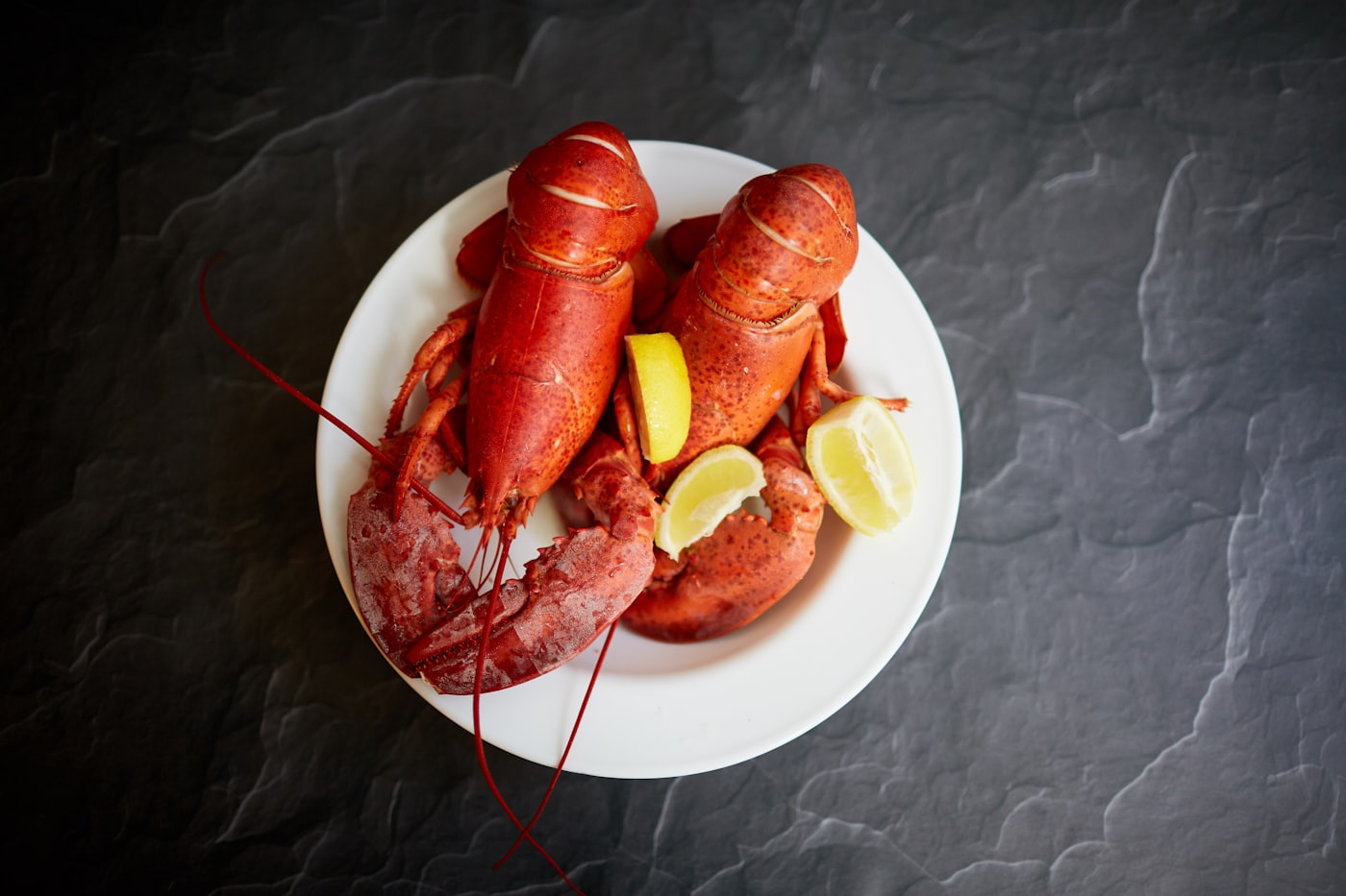 Two steamed whole lobsters with lemon on a white plate