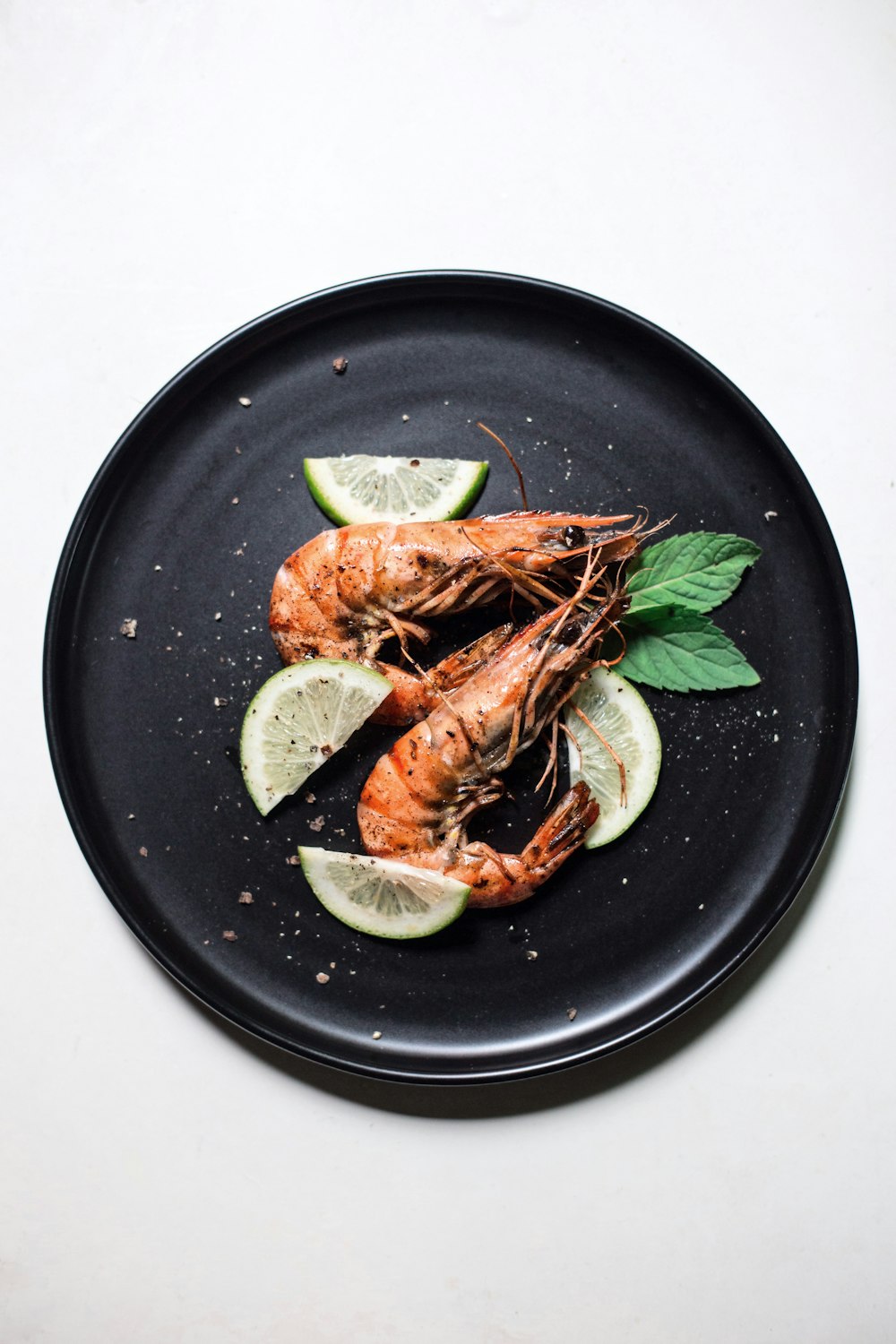 Grilled head-on prawns with lime on a black plate