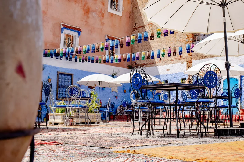 An empty blue café terrace in Chefchaouen, tables set under a white parasol