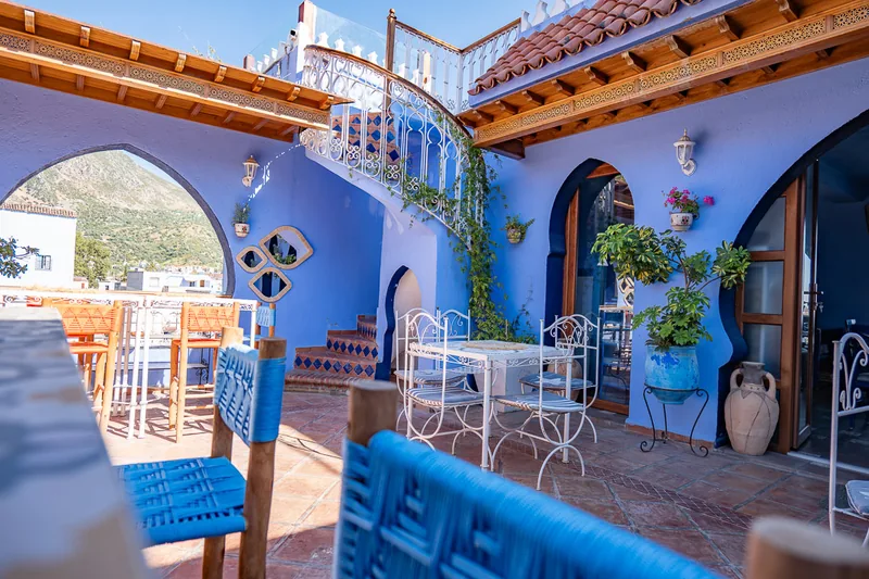 A quiet blue-painted courtyard in Chefchaouen with arches, plants and empty chairs