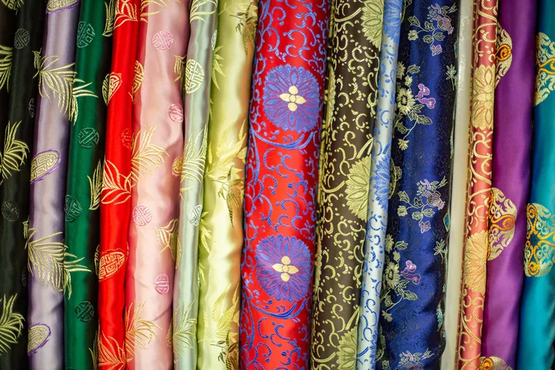 Rolls of embroidered silk in jewel colours standing side by side in a market stall