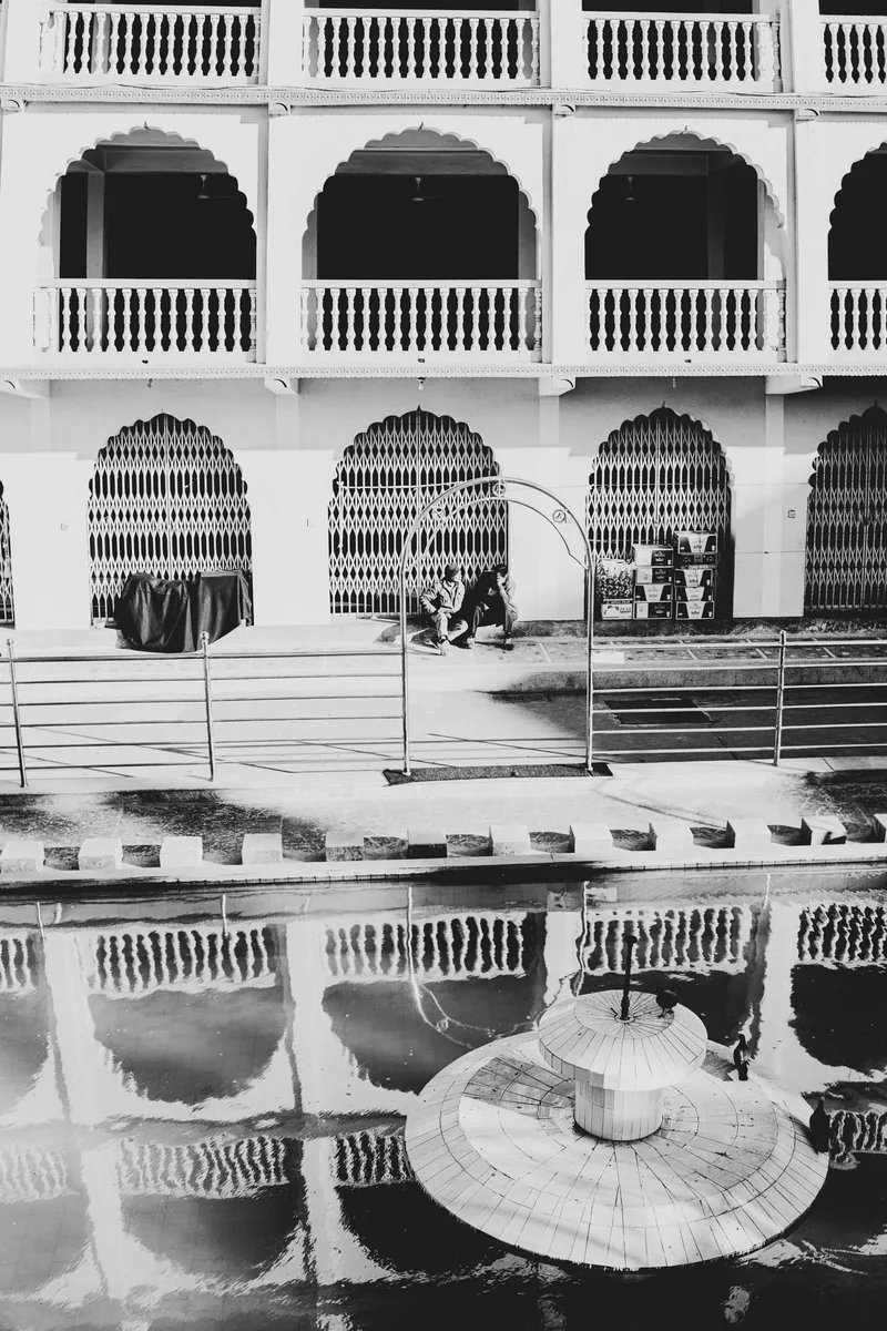 Black and white study of a tiered colonial building with repeating arches reflected in water
