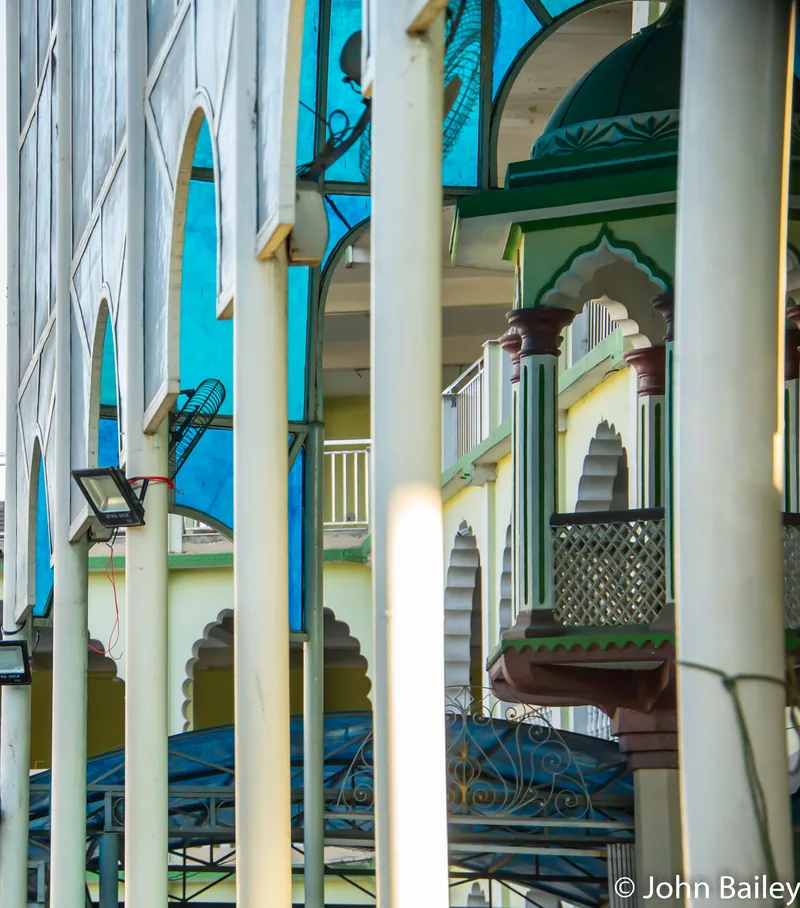 A colonnade of white and cyan columns and arches receding in bright sunlight