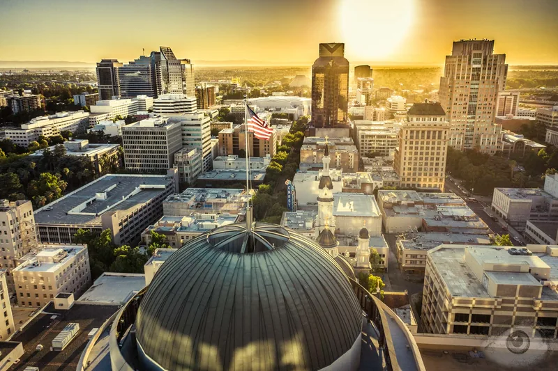 Aerial view over a downtown at golden hour, a domed roof catching the last of the sun