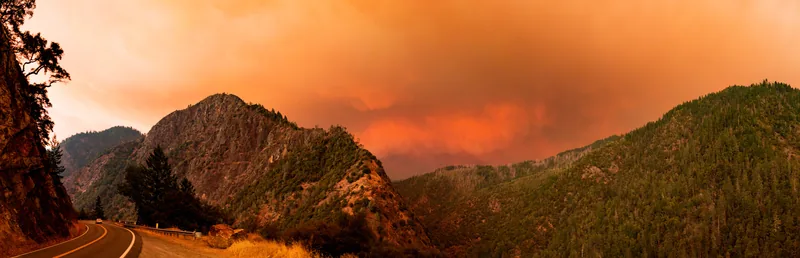 An empty mountain road curving through hills under a burning orange sunset sky