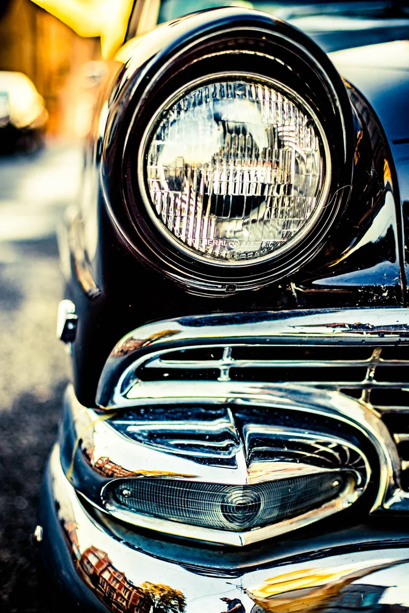 Tight detail of a chrome headlight and curved fender on a classic American car