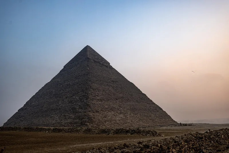 The Great Pyramid of Giza in soft evening light, its stepped stone flank rising against a pale sky