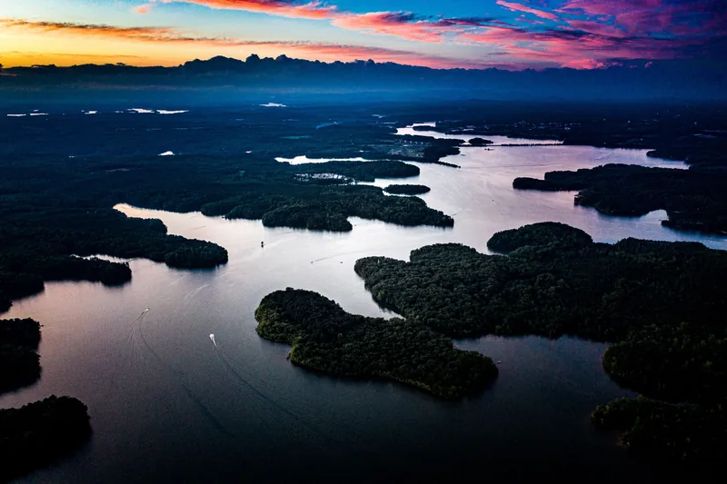 Aerial view at dusk of scattered mangrove islands in dark still water, pink sky reflected