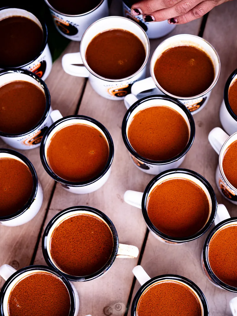 Overhead view of a dozen small glass cups of chai arranged on a metal tray