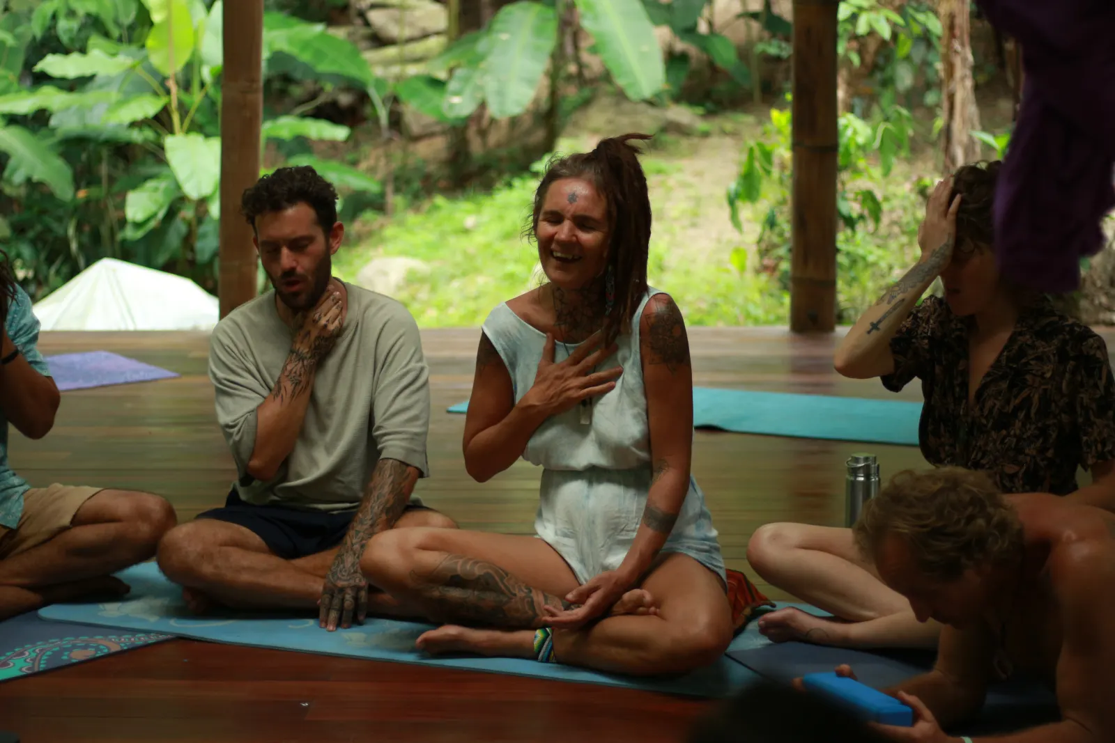 People sitting in a circle on the shala floor, laughing, hands on hearts
