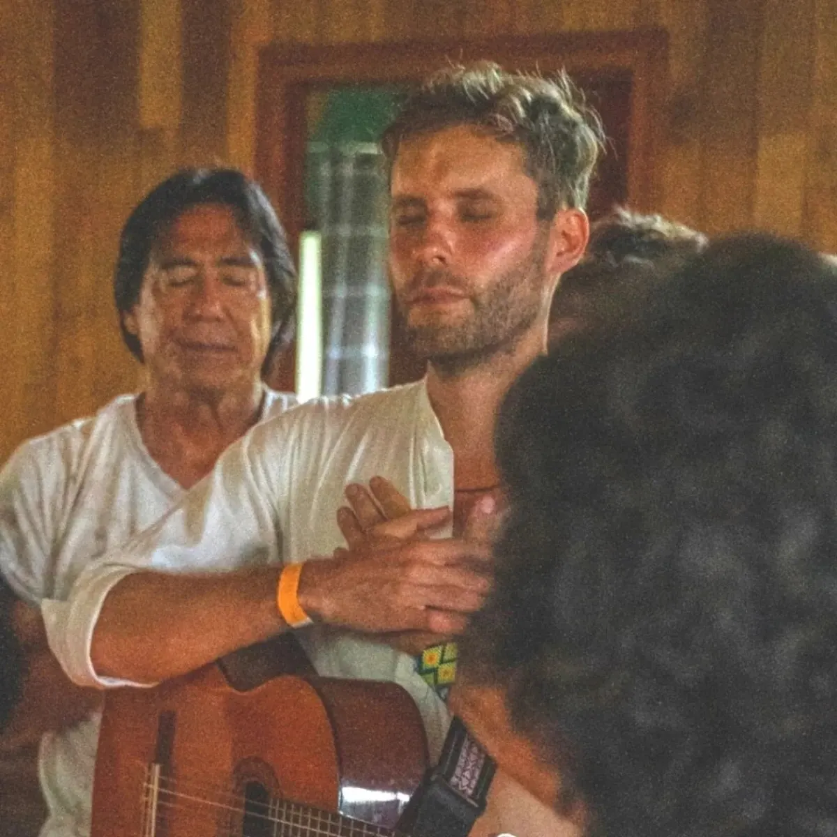 Two men embracing in the lodge, one holding a guitar